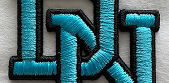 Interlocking blue custom embroidered letters D and N on a white shirt.