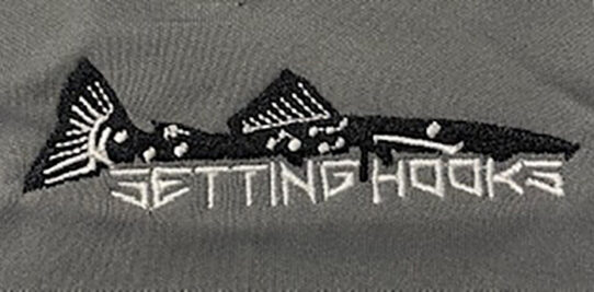 Black and white embroidered fish and white embroidered setting hooks logo on a gray shirt.