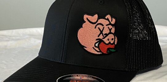 Black custom embroidered baseball hat with a pig eating an apple.